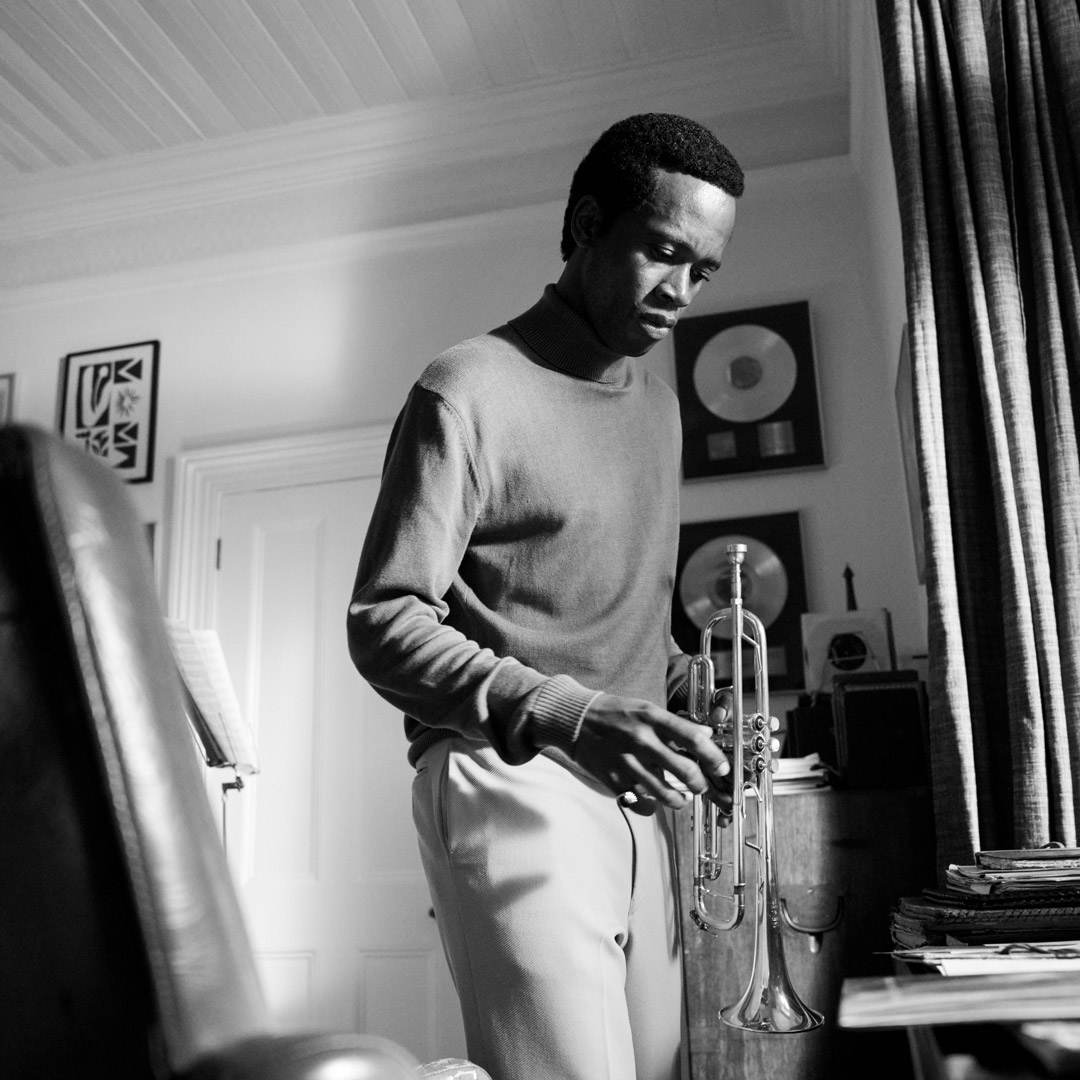 Grayscale photo of same musician holding trumpet at home