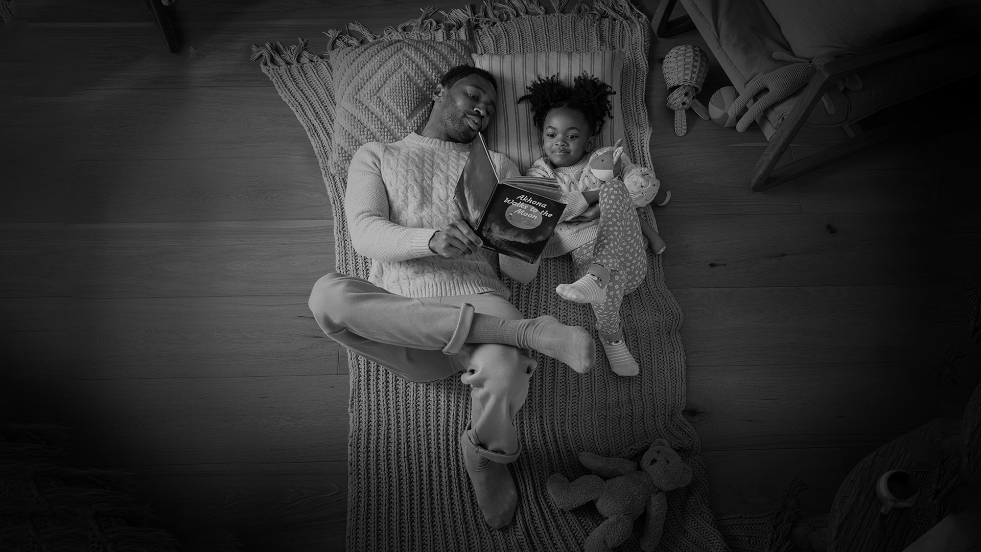 Grayscale photo of parent reading to their young child